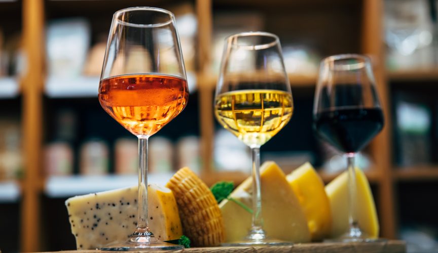 Glasses of Wine and cheese. Assortment or various type of cheese and wine glasses on the table in restaurant. Red, rose and yellow wine or champagne on the table.